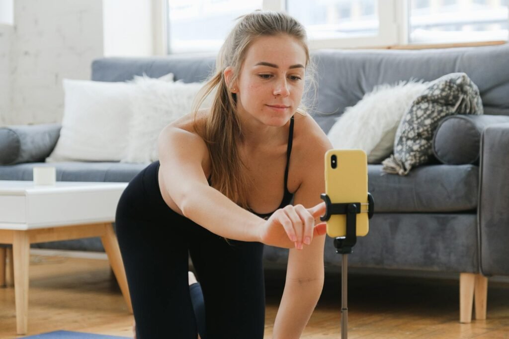 Young woman in activewear vlogging her yoga practice at home using a smartphone on a tripod.